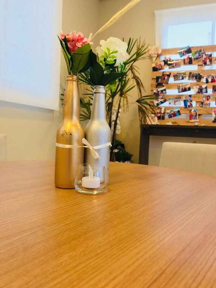 Garrafinhas pintadas com spray dourado e prateado com flores, e vela para decoração das mesas